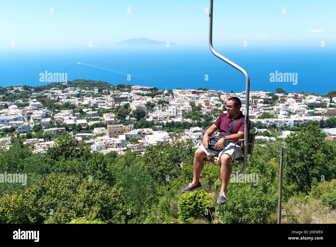 Un uomo in sella alla seggiovia fino alla cima del monte solaro sull'isola di capri e il golfo di Napoli, Italia. Foto Stock