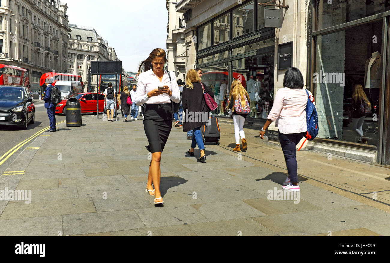 Business donna cammina lungo una strada a Londra in Inghilterra mentre a guardare nel suo telefono cellulare. Foto Stock