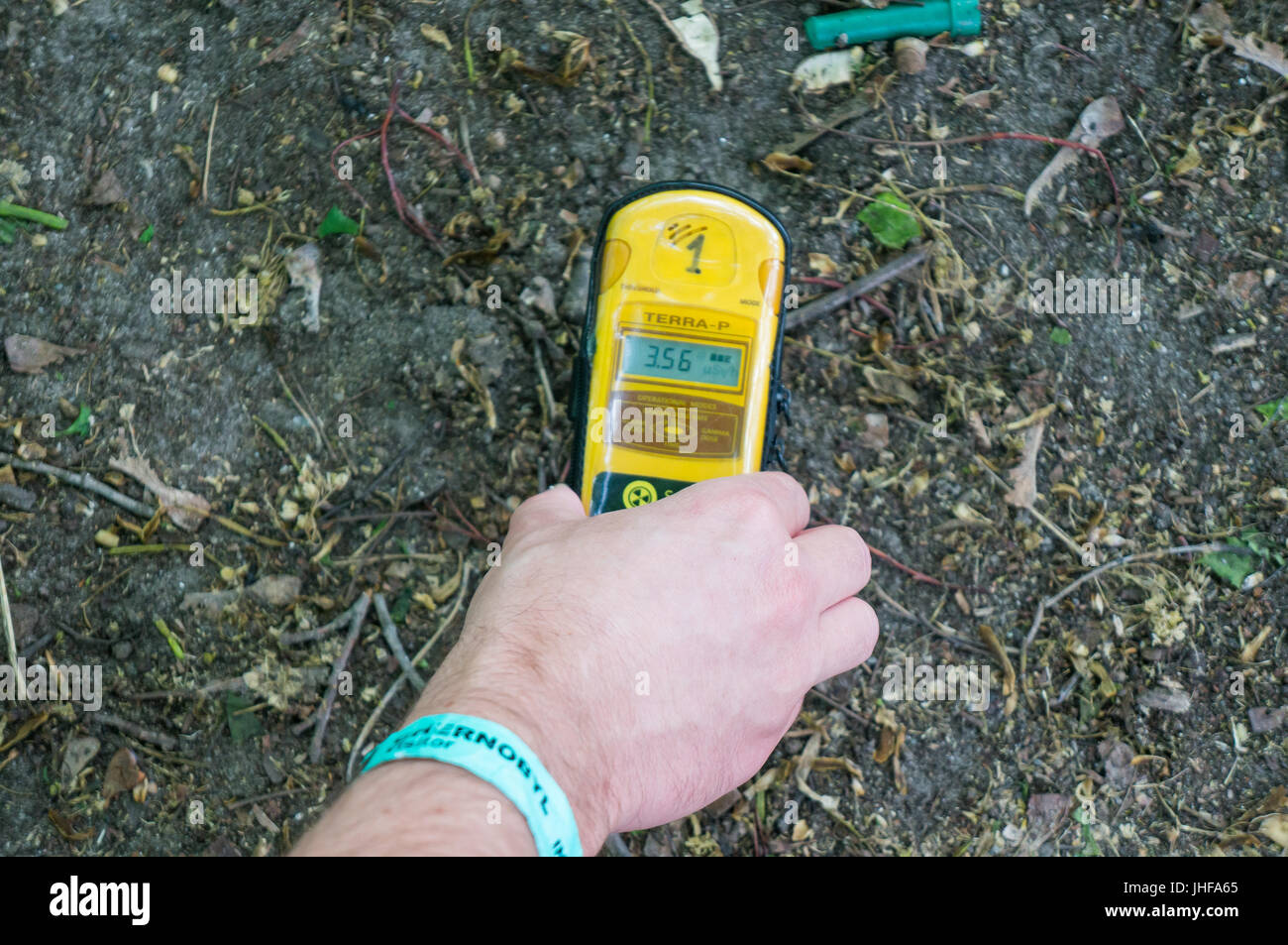 Mano che tiene un contatore Geiger sullo sporco pavimento coperto di Chernobyl Foto Stock