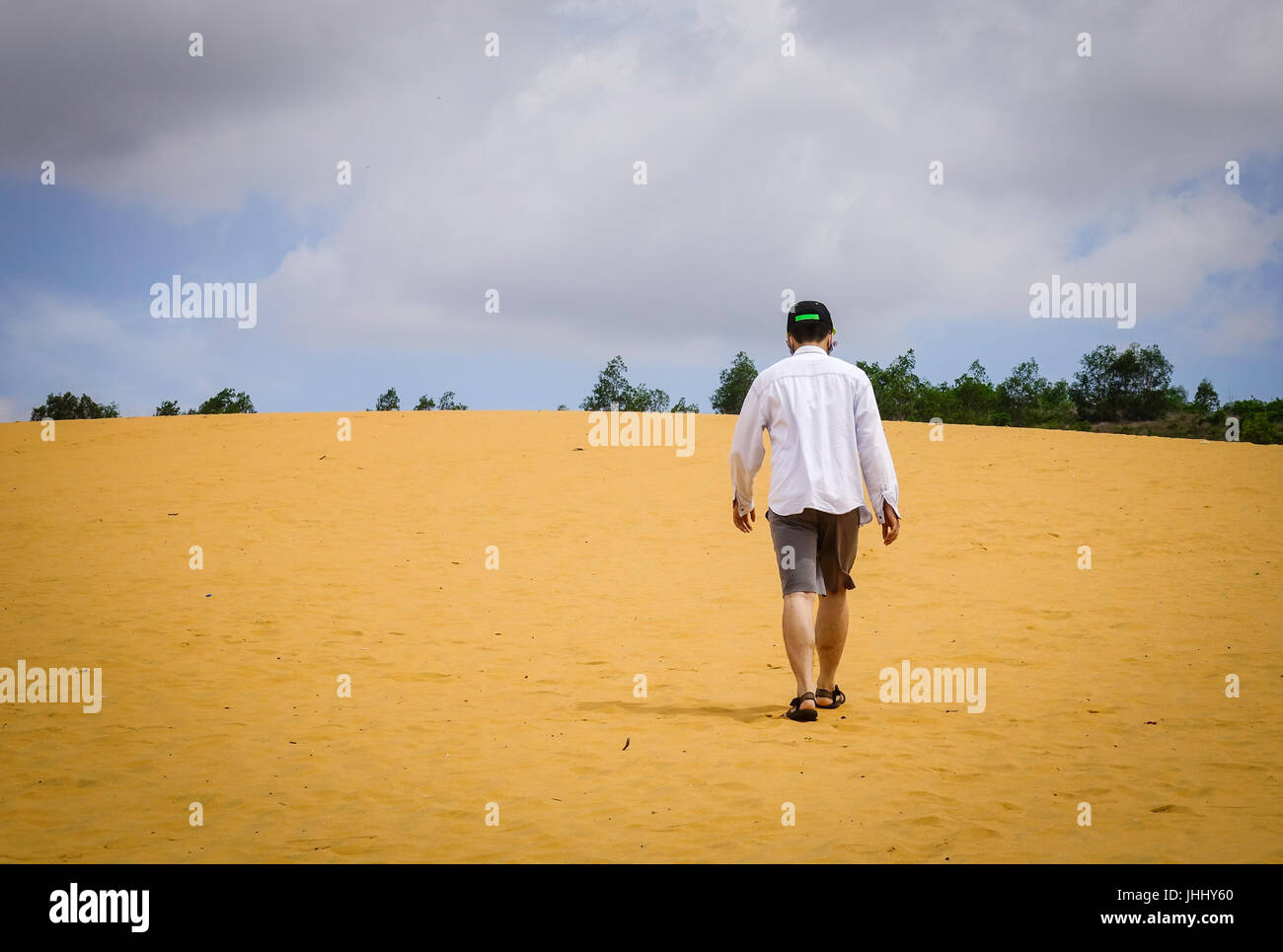 Un giovane uomo a camminare sulle dune di sabbia a giornata soleggiata in Mui Ne, Vietnam. Dune di sabbia appena fuori di Mui ne sono uno del Vietnam affascinante odditi geologica Foto Stock