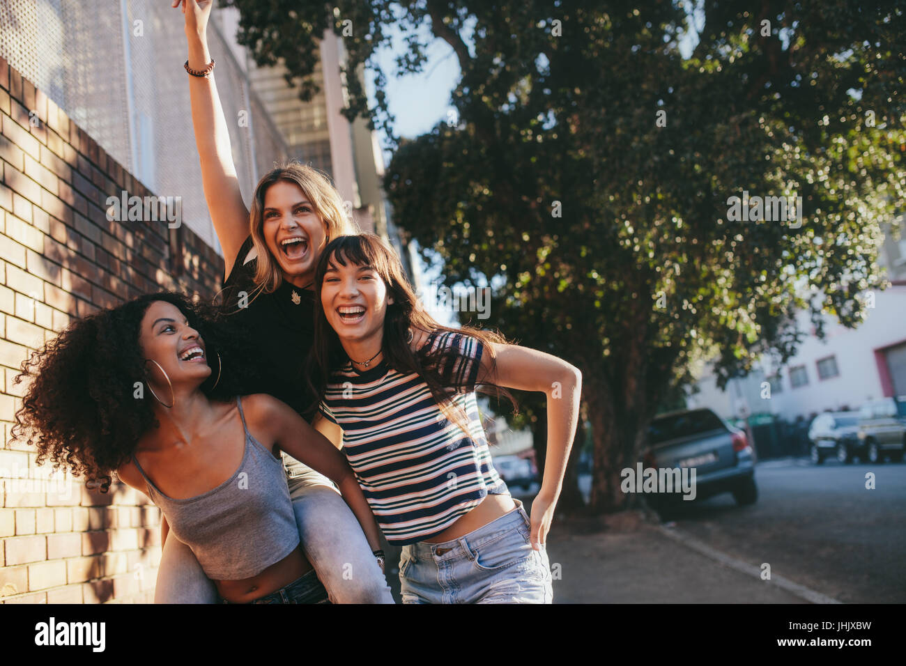 Colpo all'aperto di multi etnico amici femmina passeggiate all'aperto in città e divertirsi. Tre giovani donne in cammino insieme, piggybacking e godendo. Foto Stock
