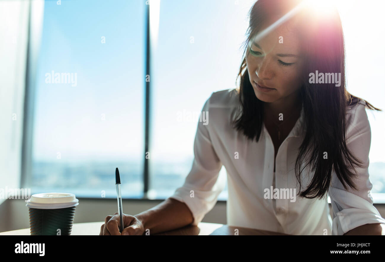 Donna giovane imprenditore lavora ad una tavola rotonda in ufficio. Femmina executive business rendendo i piani aziendali con una tazza di caffè sulla sua tavola. Foto Stock