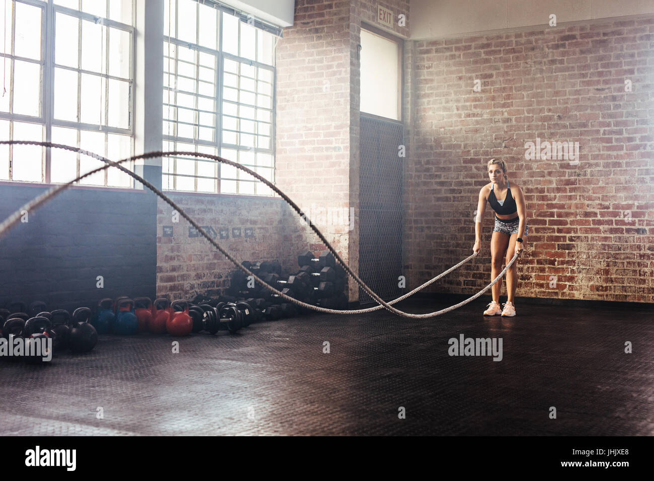 Donna che utilizza la formazione di corde di esercizi in palestra. Atleta muovendo le corde in moto ondoso come parte della forza di formazione. Foto Stock