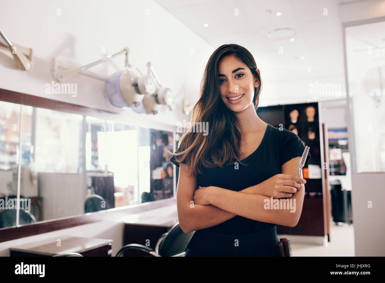 Professional donna parrucchiere in salone con le forbici in mano. Sorridente giovane donna in piedi in salone con mani piegate. Foto Stock
