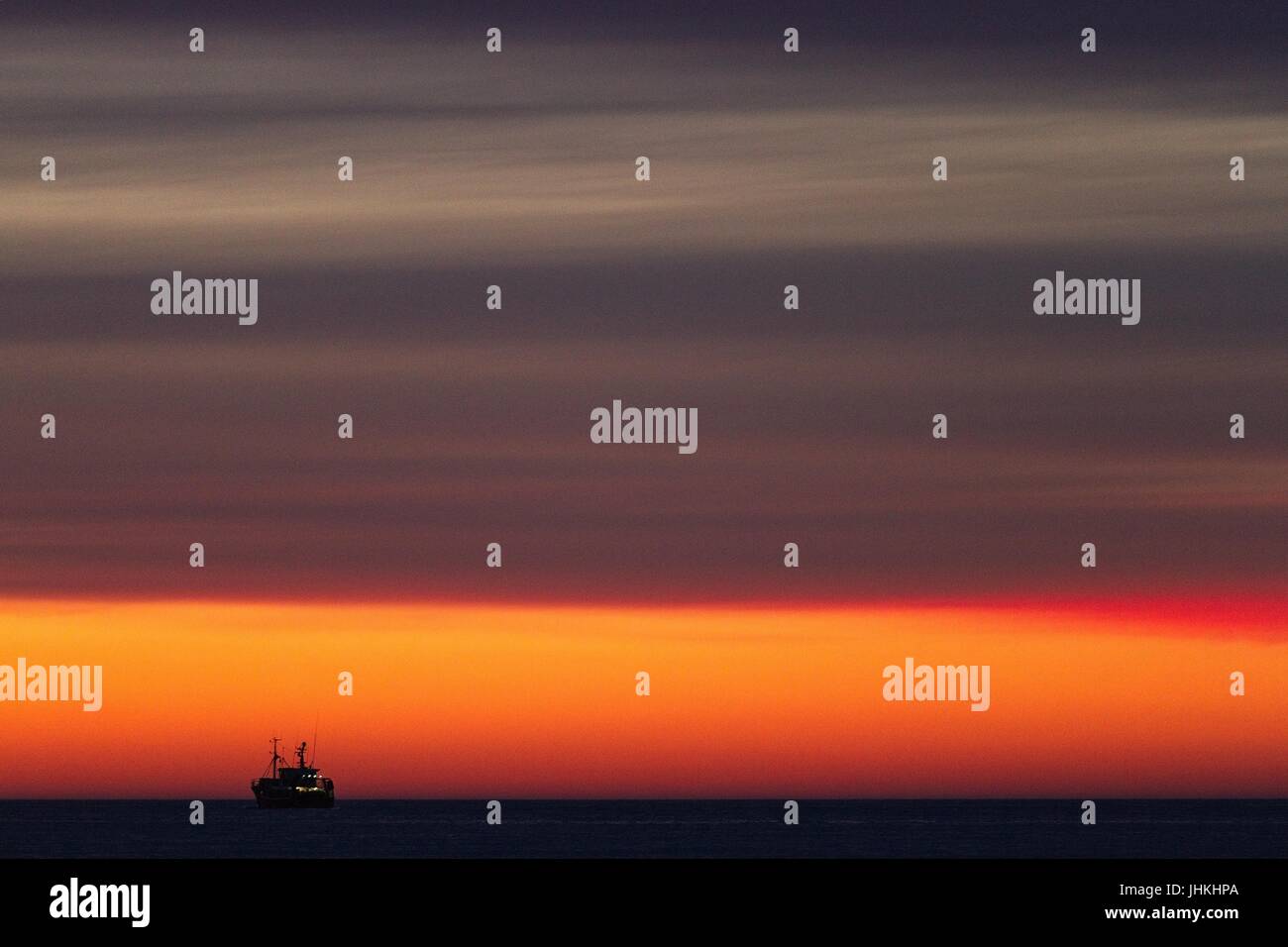 Silhouette della barca da pesca sul mare appena dopo il tramonto. Giallo dorato di colore rosso. Cielo di nuvole. Alcuni indicatori sulla barca da pesca. Foto Stock