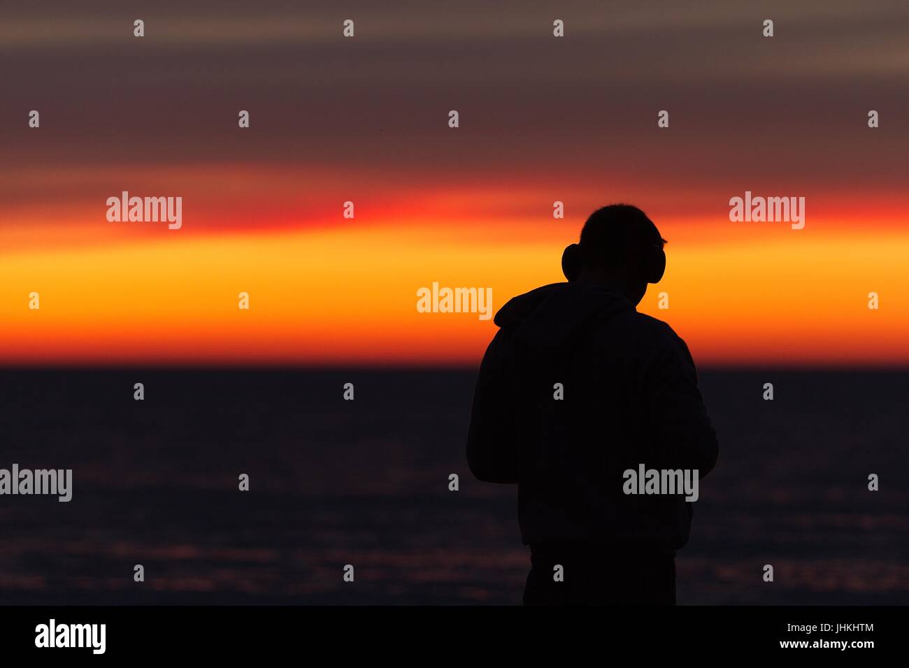 Silhouette dell uomo nella cuffia / Cuffie / auricolari durante il tramonto al mare Foto Stock