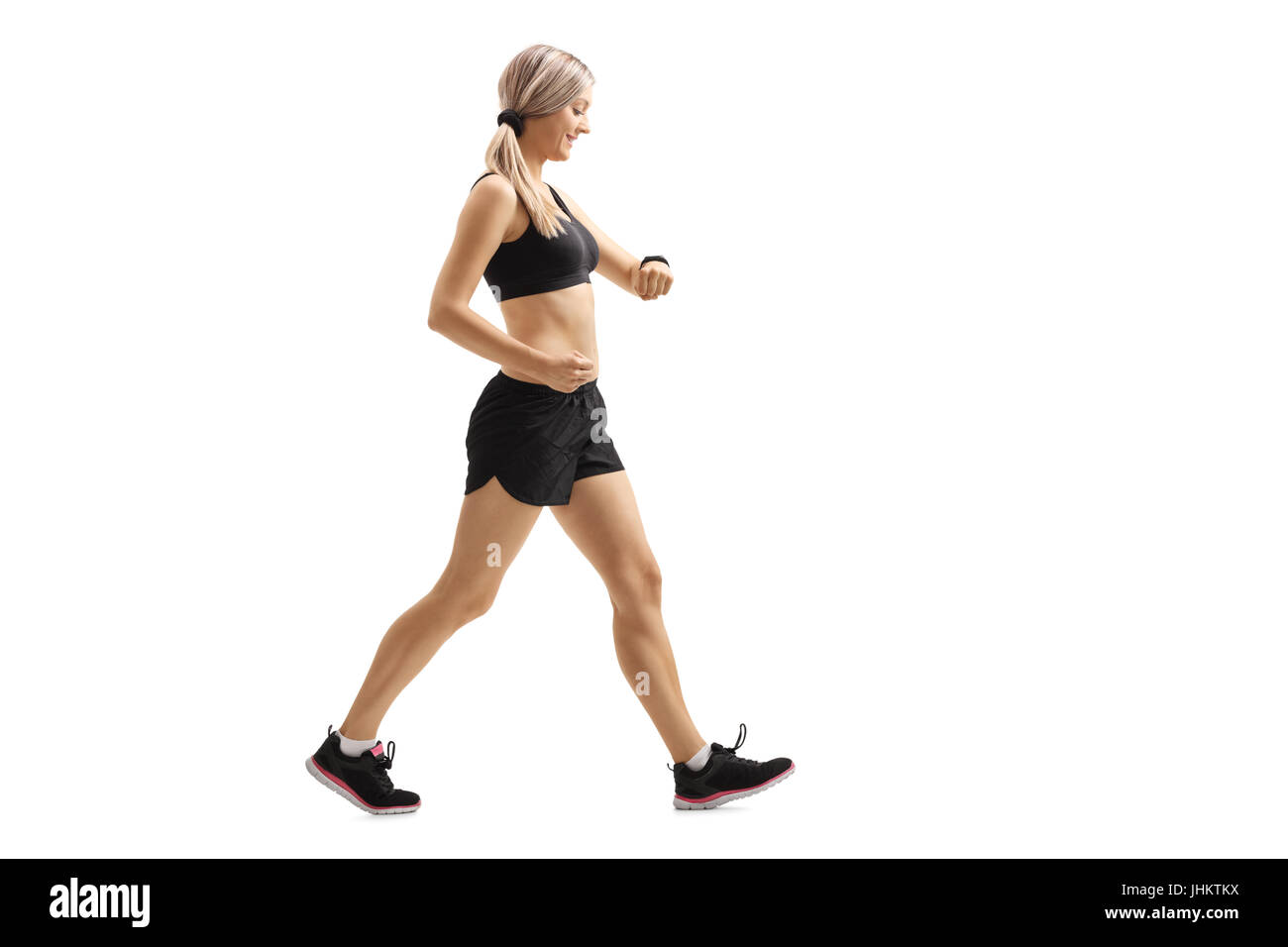 Lunghezza piena ripresa del profilo di una donna che cammina e controllando il suo orologio sportivo isolati su sfondo bianco Foto Stock