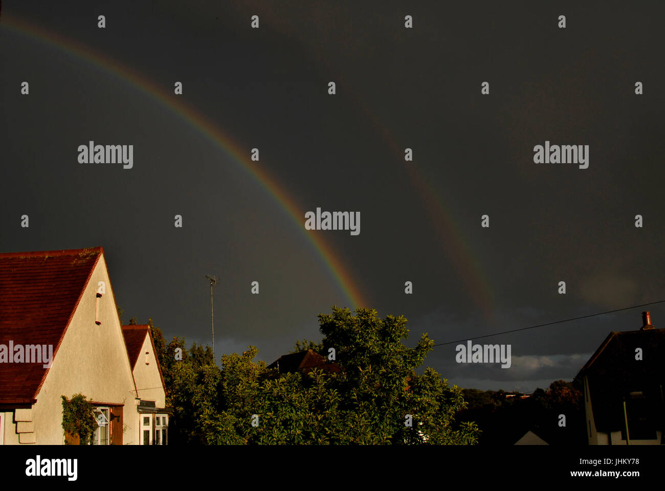 Doppio arcobaleno e nuvole scure su case suburbane Foto Stock