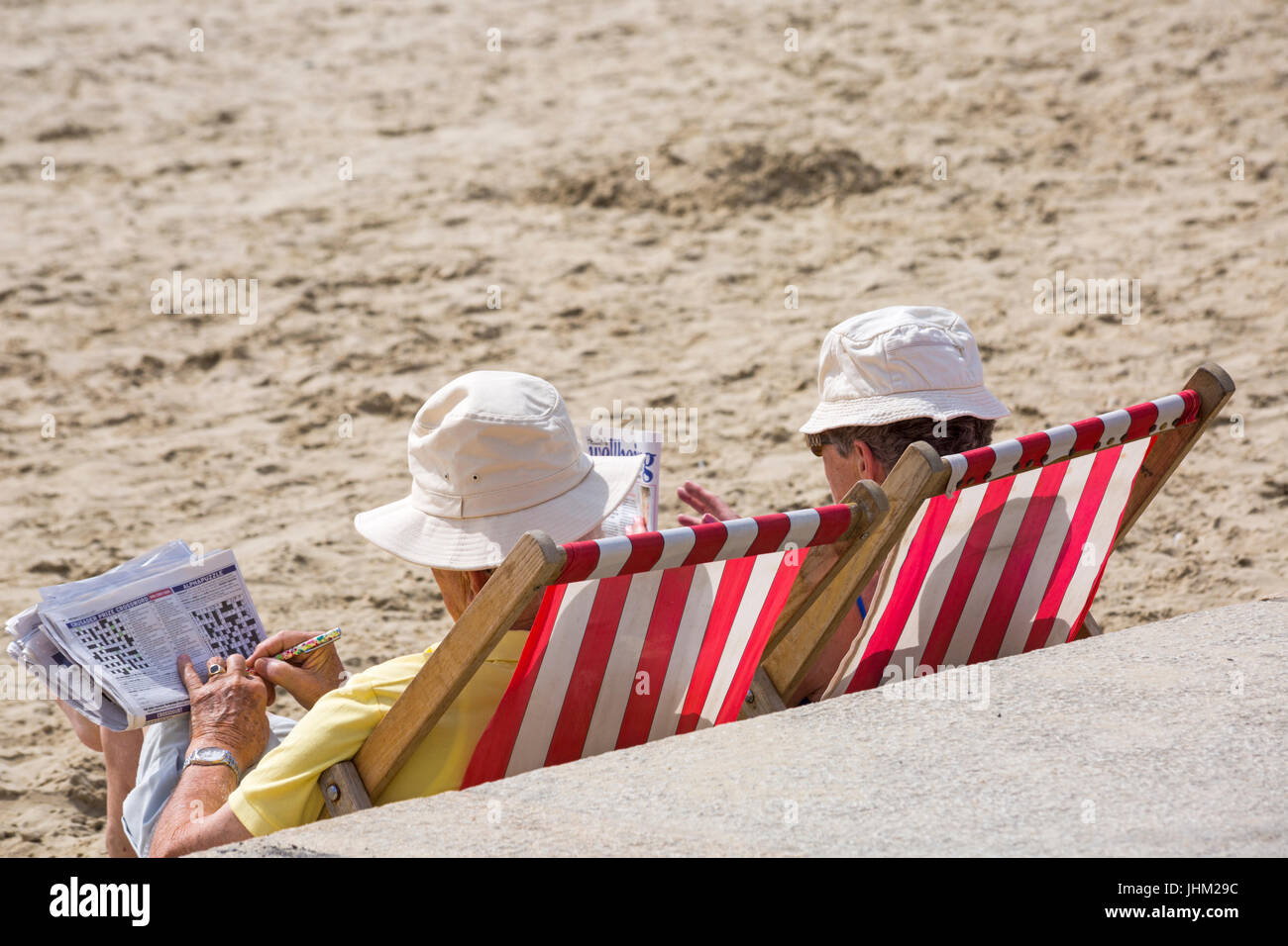 Giovane seduto in sedie a sdraio sulla spiaggia facendo cruciverba e  guardando il magazine a Lyme Regis, Dorset in luglio Foto stock - Alamy