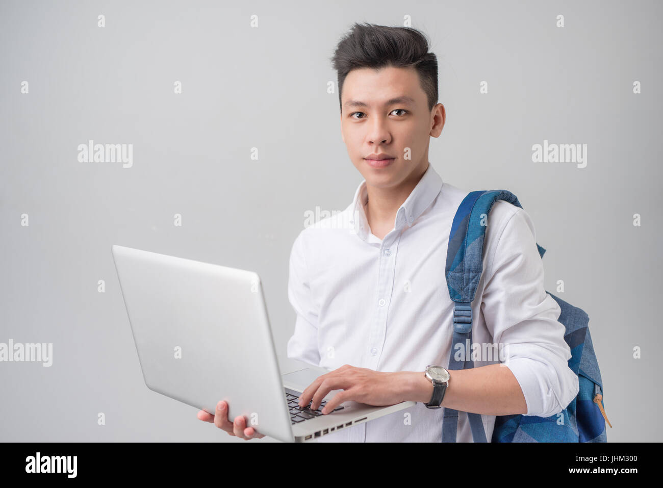 Felice casual maschio asiatici studente utilizzando computer portatile isolato su sfondo grigio Foto Stock