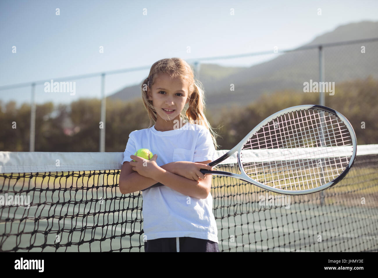Ritratto di fiducioso ragazza con racchetta da tennis e la sfera a corte durante la giornata di sole Foto Stock