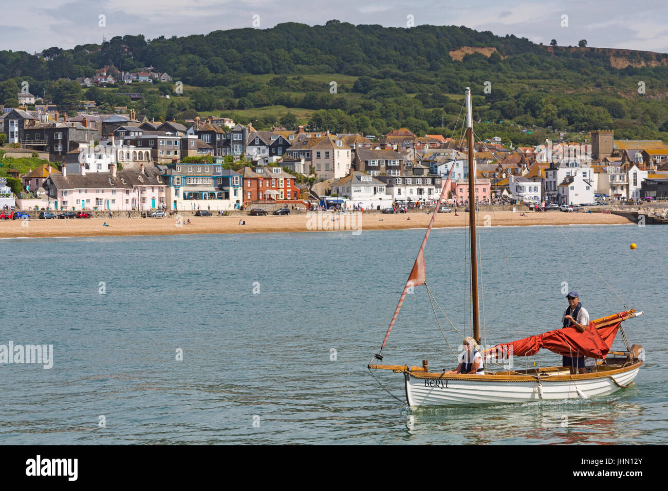 Coppia matura prendendo Beryl barca nel porto di Lyme Regis con la spiaggia e la città di Lyme Regis in lontananza, Dorset UK nel mese di luglio Foto Stock