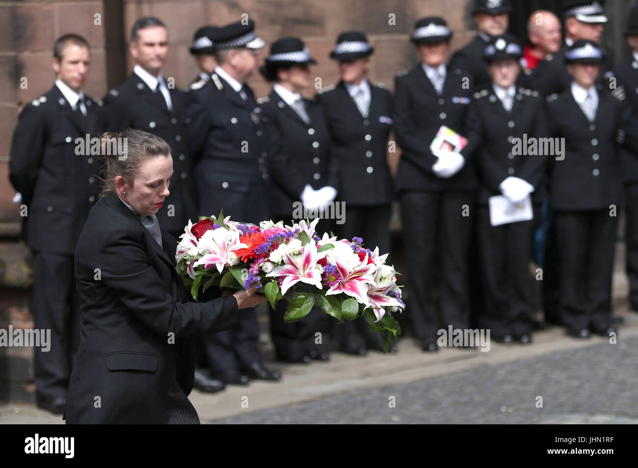 Gli ufficiali di polizia guarda come i fiori sono portati al di fuori di Chester Cathedral seguendo il servizio funebre del detective Constable Elaine McIvor, 43, a che serve il Cheshire Constabulary ufficiale che è stato ucciso nell'Arena di Manchester il bombardamento di attacco terroristico. Foto Stock