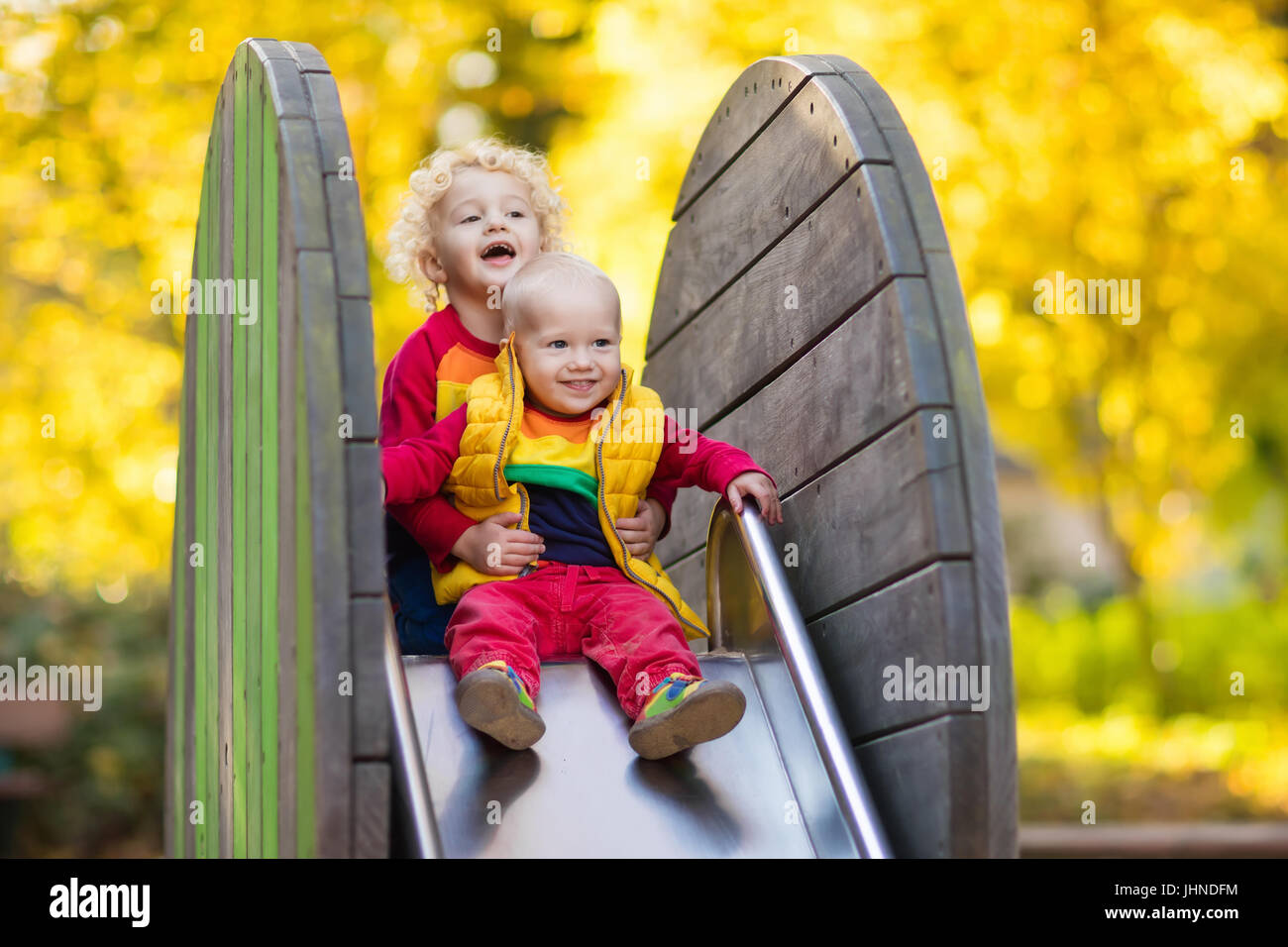 Bambini sul parco giochi bambini giocare nel parco d'autunno. Bambino sulla slitta e rotazione sulla soleggiata giornata di caduta. Scuola materna o asilo nido cantiere. Assistenza per bambino. Ba Foto Stock