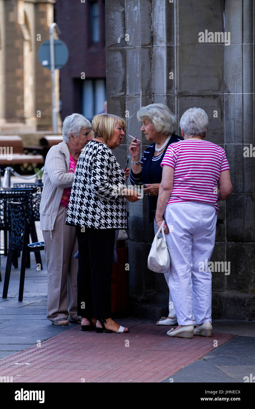 Quattro donne anziane assieme al di fuori di un pub locale in chat e avente un fumo a Dundee, Regno Unito Foto Stock