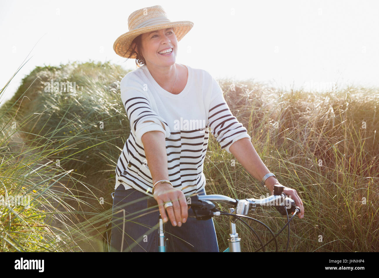 Sorridente donna matura Bicicletta Equitazione sulla spiaggia soleggiata percorso di erba Foto Stock