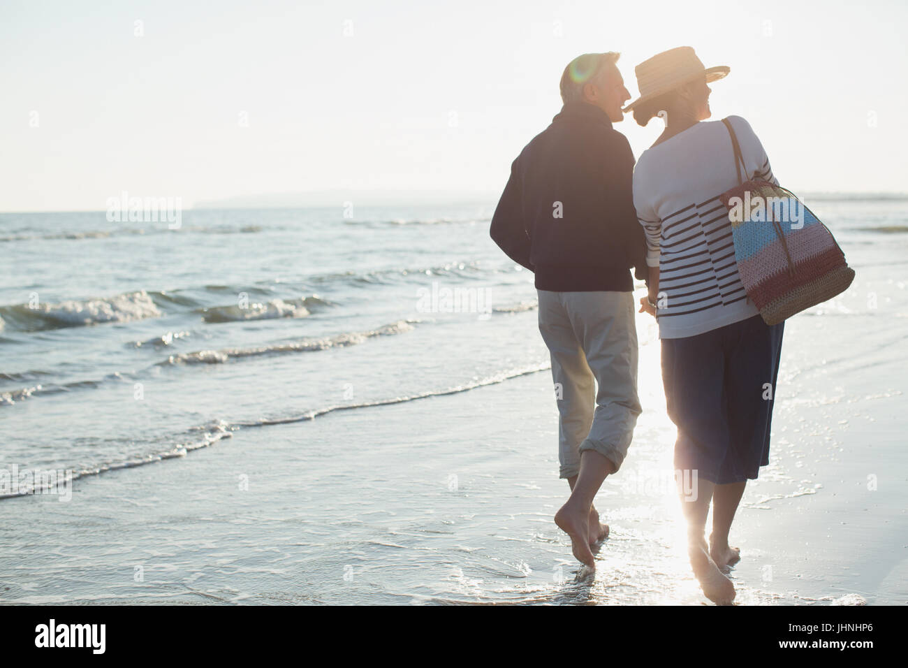 A piedi nudi coppia matura passeggiate sulla spiaggia al tramonto Foto Stock