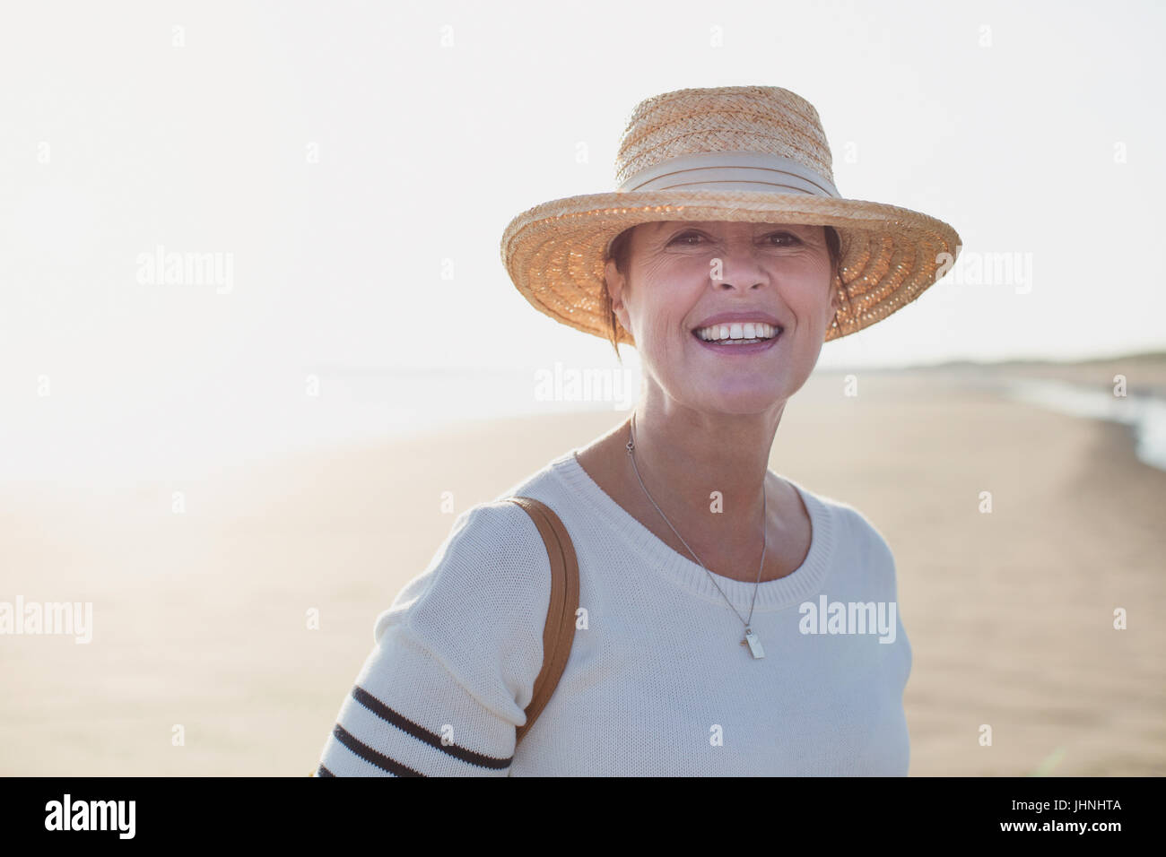 Ritratto sorridente donna matura indossando cappello di paglia sulla soleggiata spiaggia di estate Foto Stock