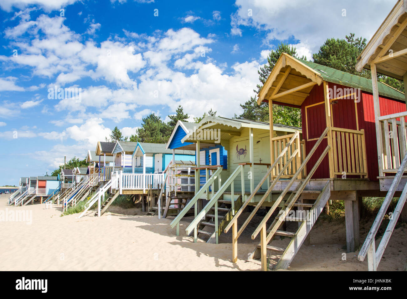 Colorate e cabine in legno su palafitte presso il deserta spiaggia sabbiosa di pozzetti accanto al mare in nirfolk, Regno Unito sotto un cielo blu con un sole estivo. Foto Stock
