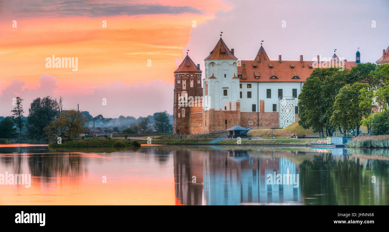 Mir, Bielorussia. Vista panoramica del complesso del Castello di Mir soleggiata sul Cielo di tramonto sullo sfondo. Vecchie Torri sono riflesse nel lago di acqua di fiume Foto Stock