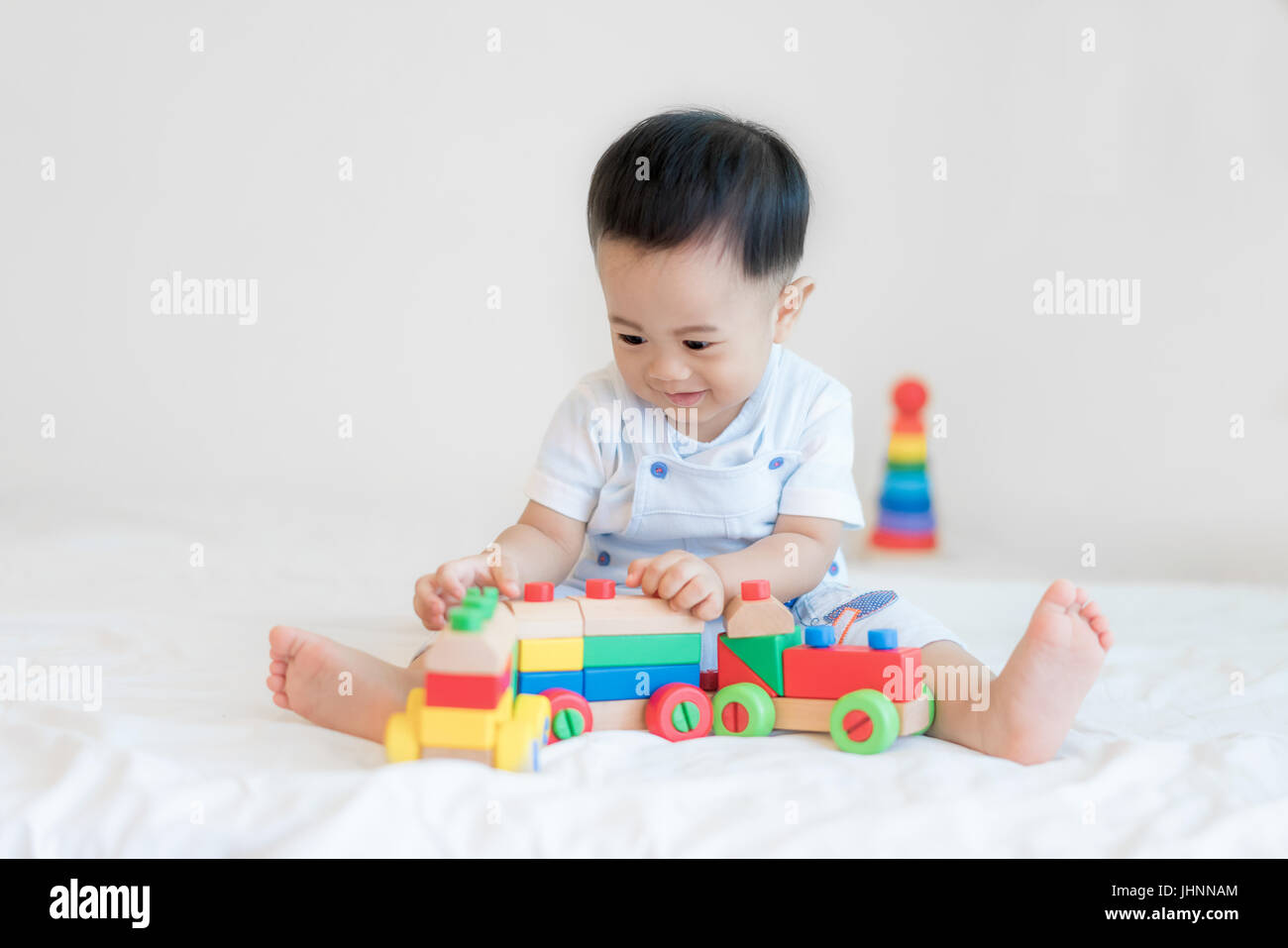 Adorabili Asian baby boy 9 mesi seduta sul letto e a giocare con i colori del treno in legno giocattoli a casa. Foto Stock