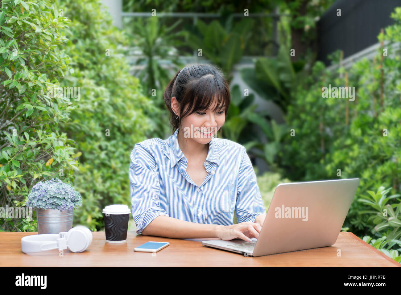 Donna asiatica in faccia sorridente con notebook, workplace nel giardino della struttura. Concetto di donna asiatica stile di vita. Foto Stock