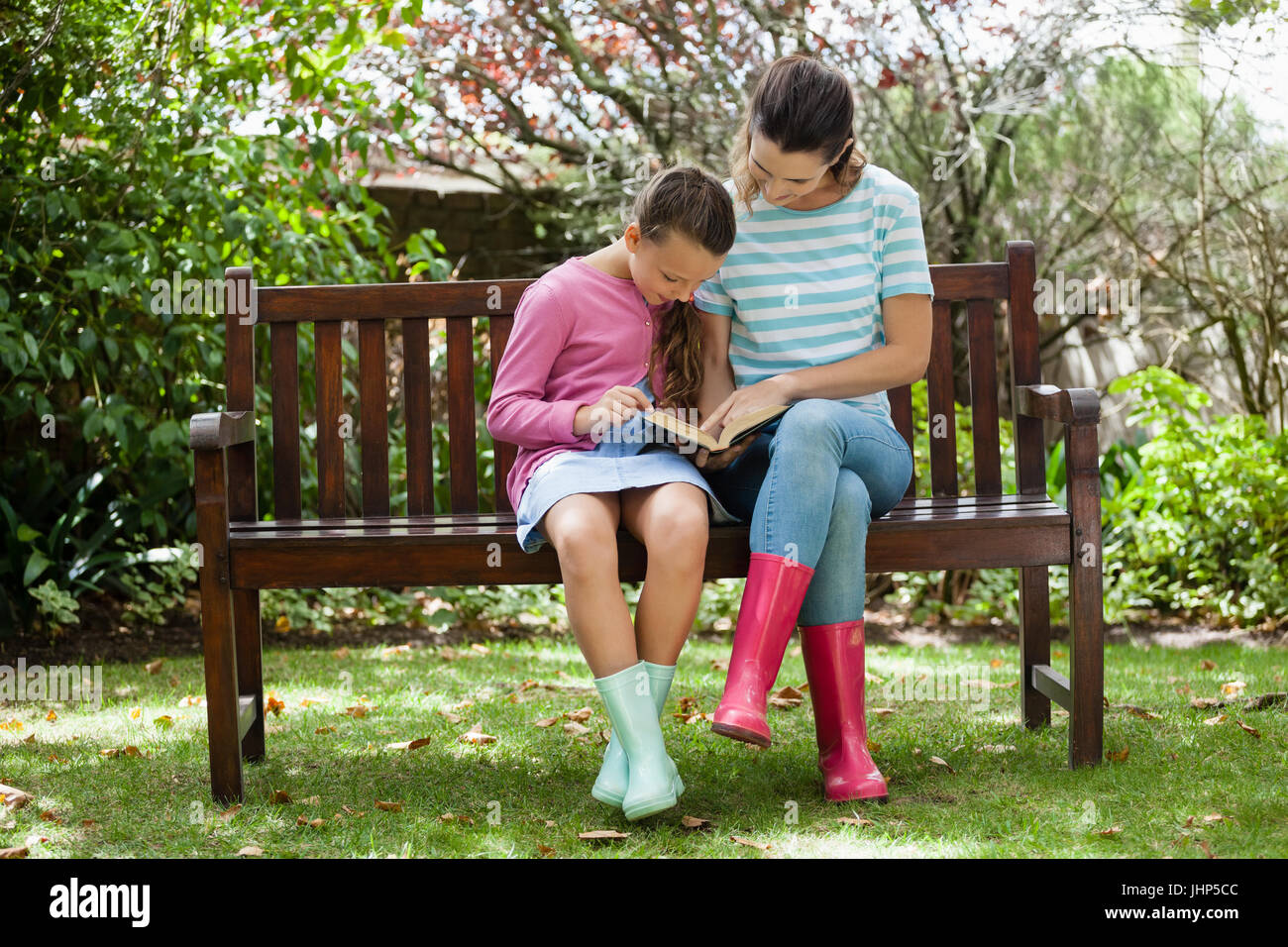 Madre e figlia romanzo di lettura mentre è seduto sulla panca di legno a backyard Foto Stock