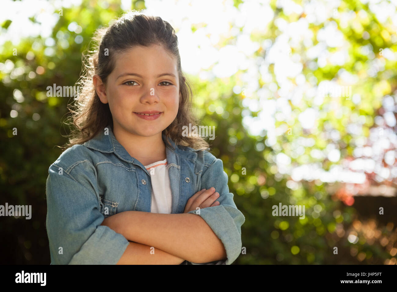 Ritratto di fiduciosi la ragazza con le braccia incrociate in piedi contro piante in cortile Foto Stock