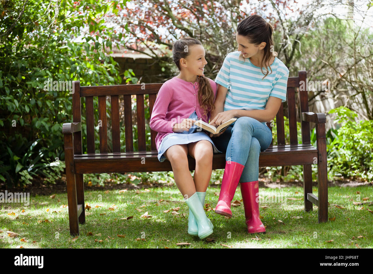 Allegro madre e figlia romanzo di lettura mentre è seduto sulla panca di legno a backyard Foto Stock