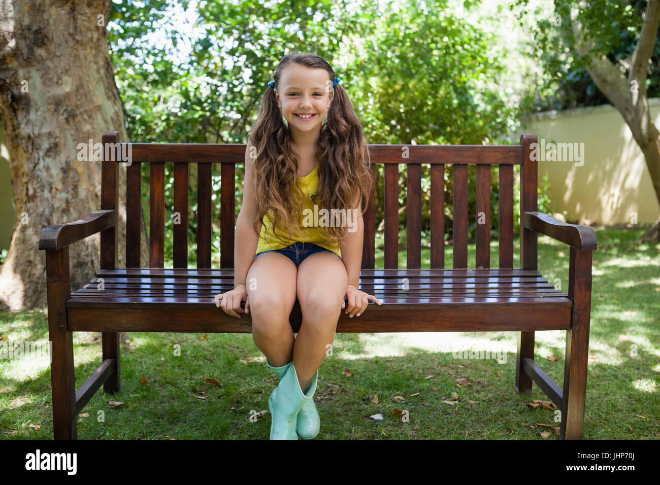 Ritratto di sorridente ragazza seduta sulla panca di legno a backyard Foto Stock