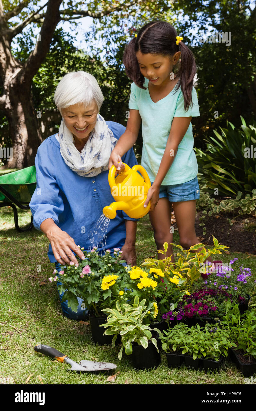 Senior donna che guarda la ragazza di fiori di irrigazione in cortile Foto Stock