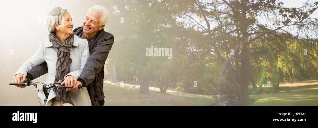 Digital composito della coppia di anziani sulla bicicletta contro sfocata park con flare Foto Stock