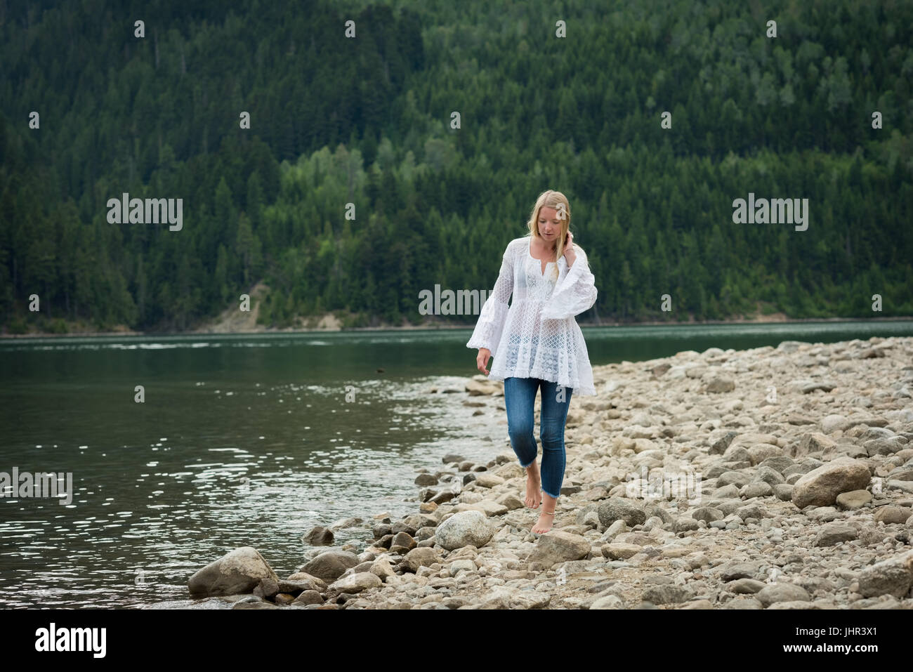 Giovane donna camminare sulle rocce a lakeshore contro alberi Foto Stock