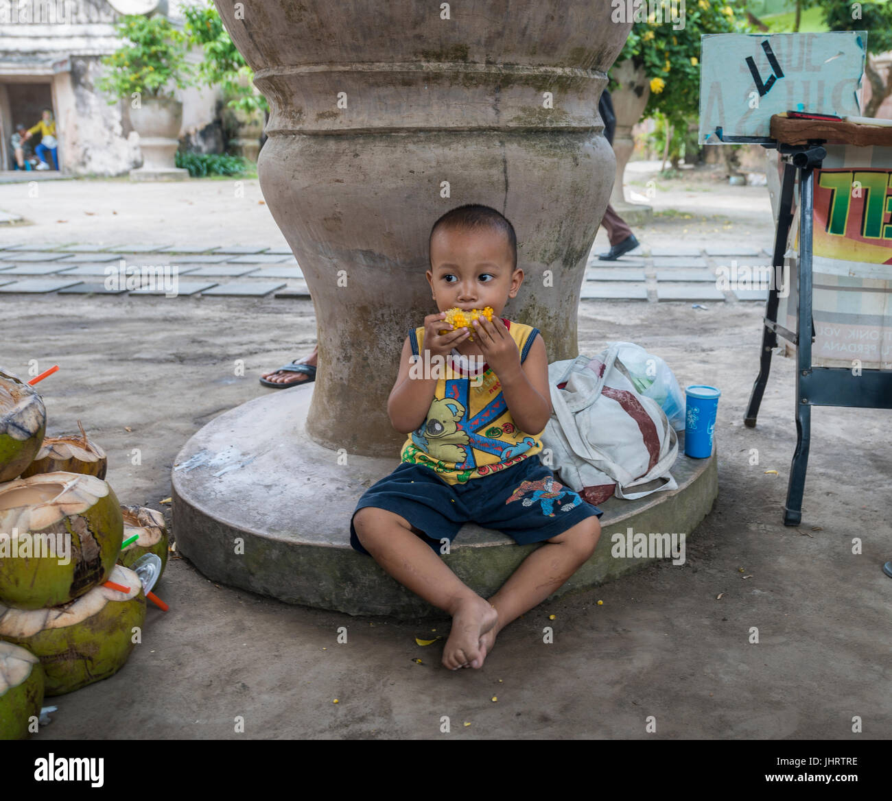 Piccolo Ragazzo indonesiano mangiare mais alla griglia sul lato strada, Yogyakarta, Java, Indonesia Foto Stock