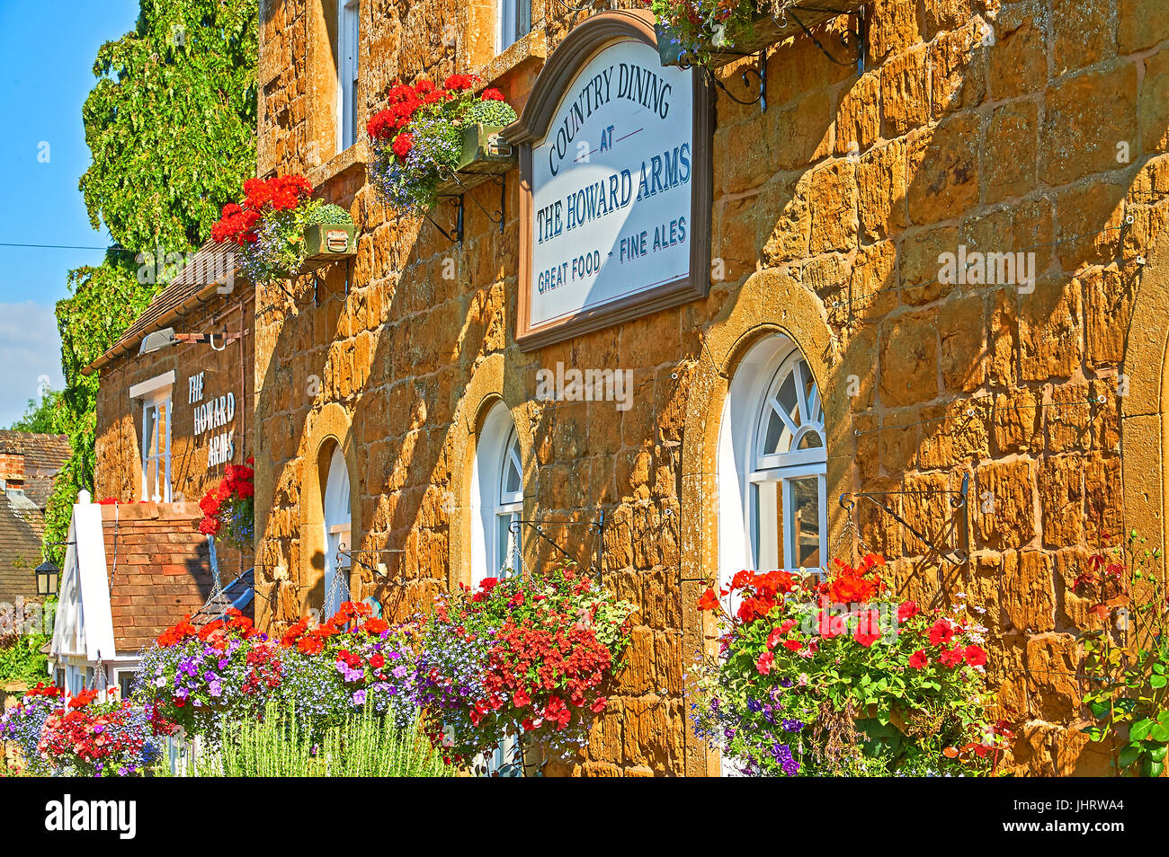 Colorati cestelli appesi sulla parte anteriore di una pietra di Cotswold public house, nel Warwickshire villaggio di Ilmington Foto Stock