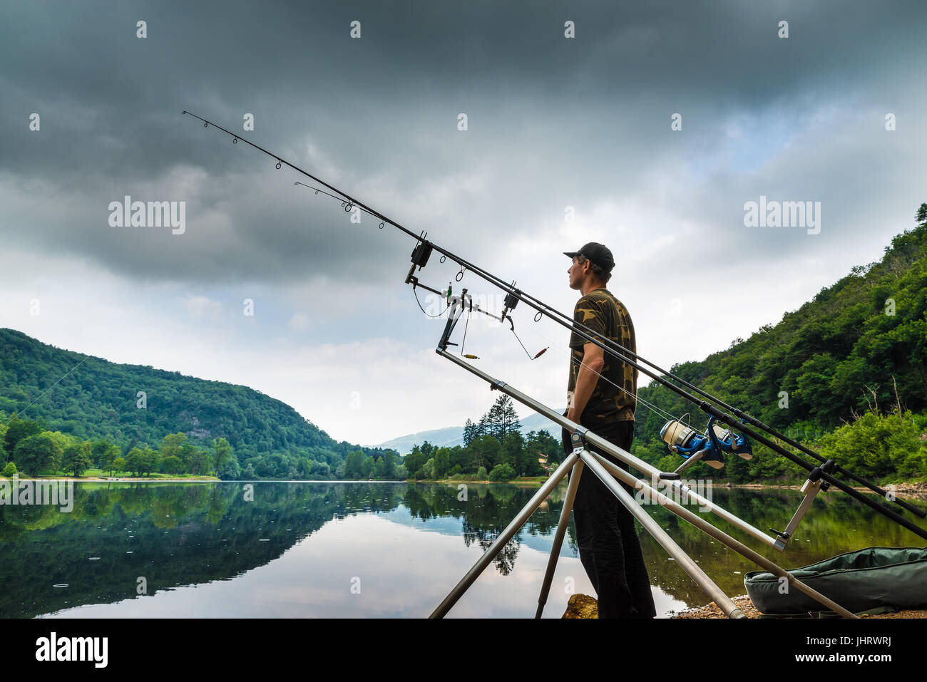 Le avventure di pesca, la pesca alla carpa. Il pescatore sulla riva di un lago in una mattinata con cielo scuro e le nuvole grigio Foto Stock
