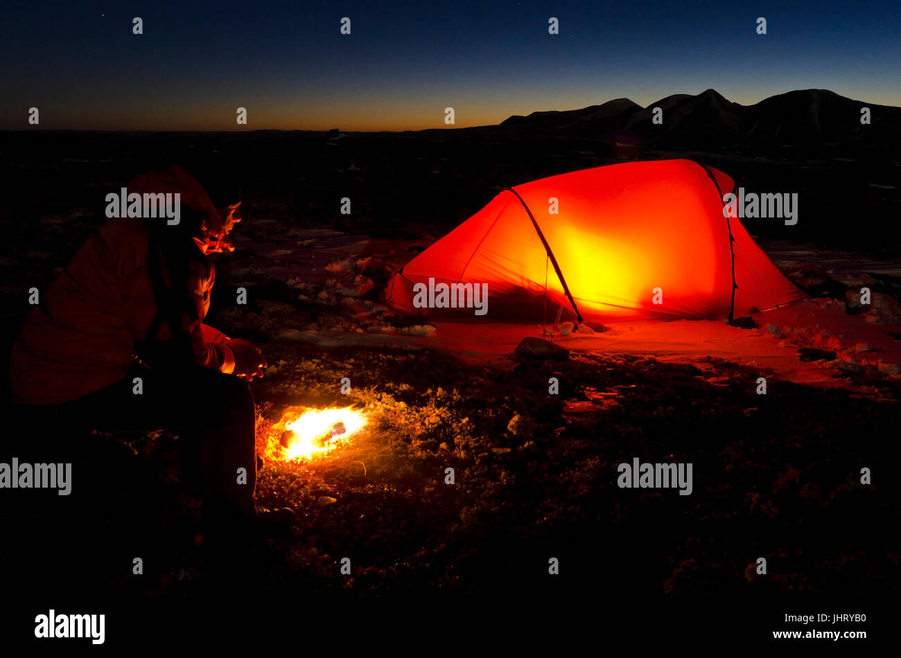 Uomo con falò e tenda illuminata, Engerdalsfjellet, sullo sfondo del vertice Rendalssoelen, Hedmark Fylke, Norvegia, ottobre 2011, Mann mit L Foto Stock