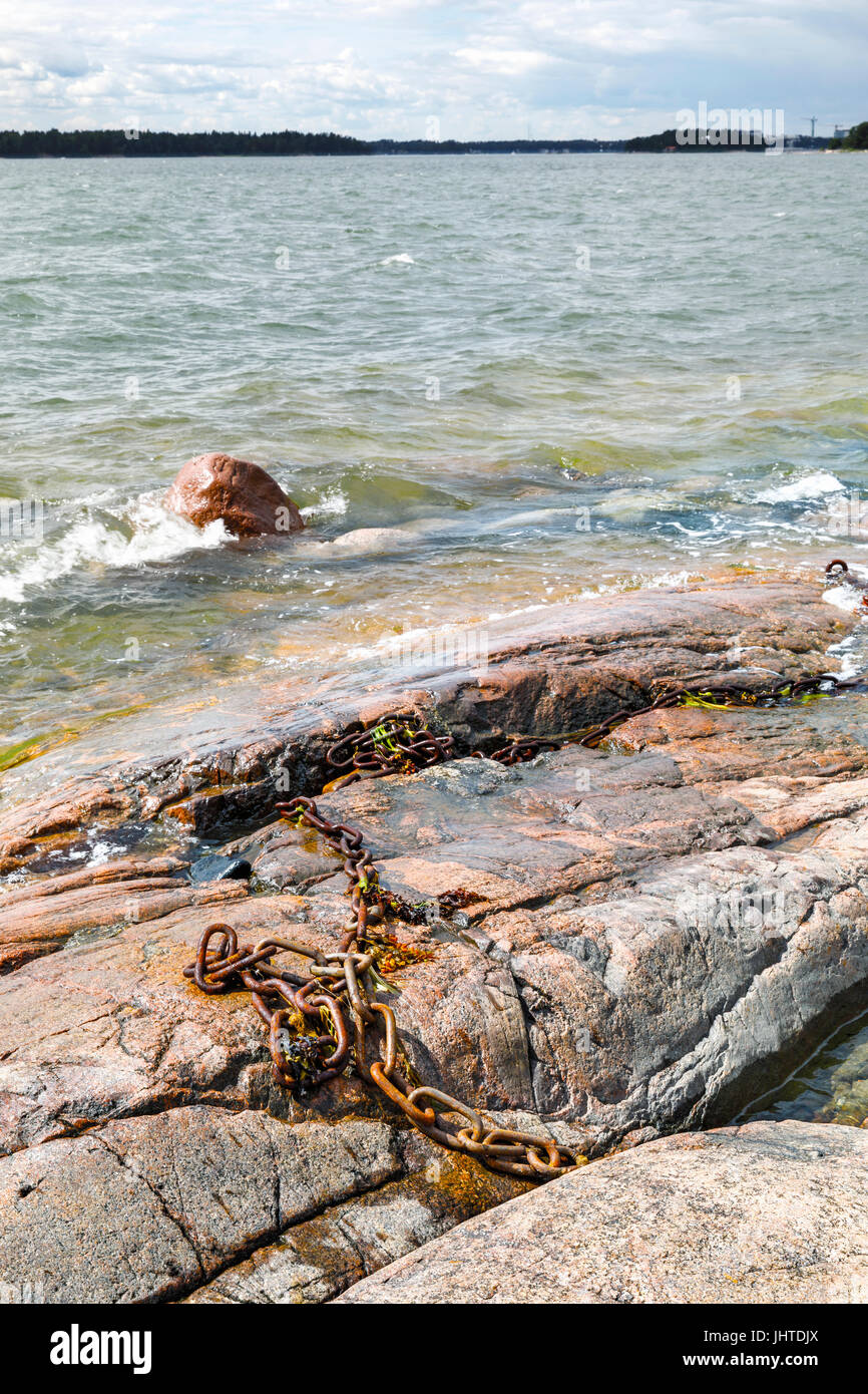 Schiumoso bianco onde acqua colpite nel litorale roccioso. Vecchio arrugginito catena di ferro sulle rocce. Foto Stock