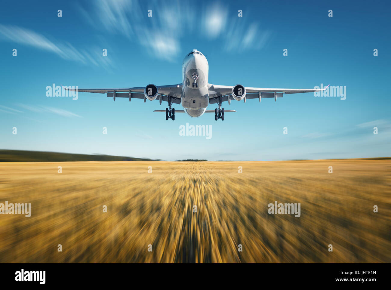 In aereo con motion blur effetto. Paesaggio con bianco aereo passeggeri è volare, cielo blu, il campo di grano al tramonto in estate. Aereo passeggeri Foto Stock