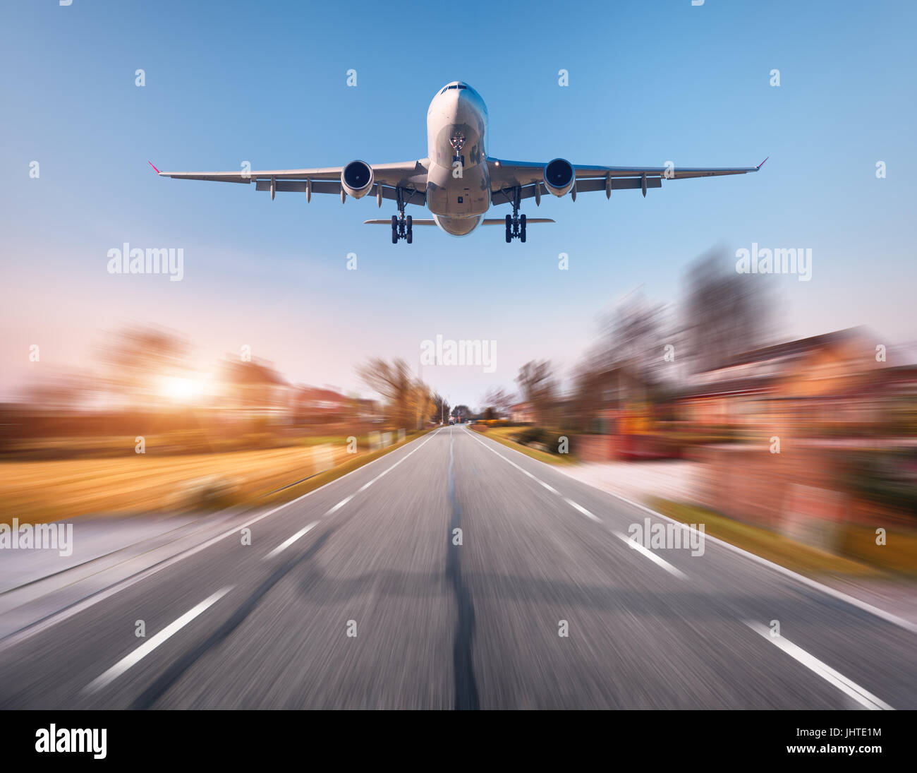 Aereo passeggeri con motion blur effetto. Aeroplano vola nel cielo di tramonto oltre le zone rurali strada asfaltata al tramonto nei Paesi Bassi. Sbarco airplan Foto Stock