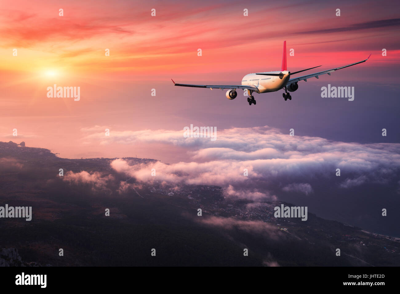 In aereo. Paesaggio con grande bianco aereo passeggeri vola nel cielo rosso sopra le nuvole al tramonto colorato. Viaggio. Aerei per il trasporto di passeggeri è terra Foto Stock