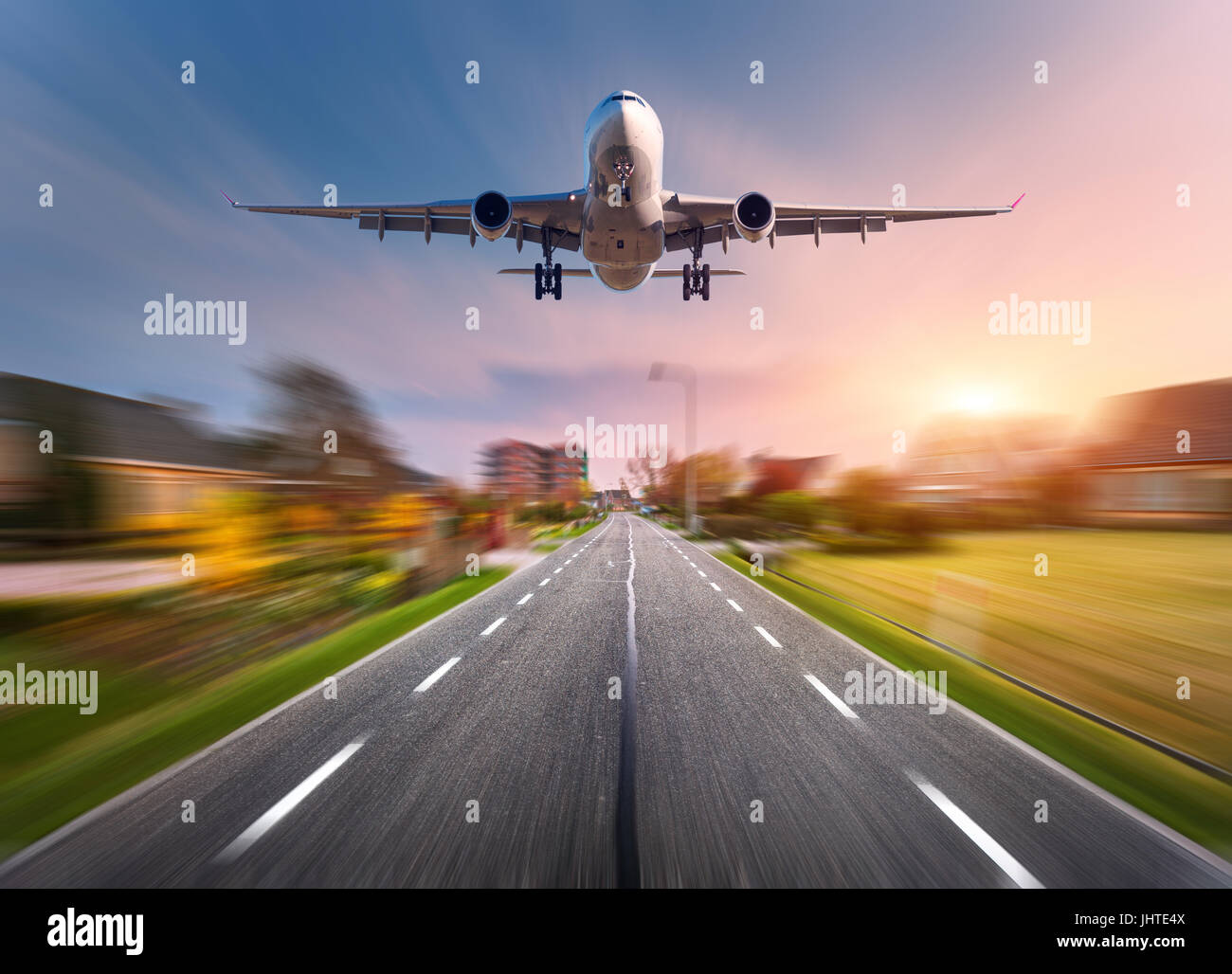 Aereo passeggeri con motion blur effetto. Aeroplano vola nel cielo di tramonto oltre le zone rurali strada asfaltata al tramonto nei Paesi Bassi. Sbarco airplan Foto Stock
