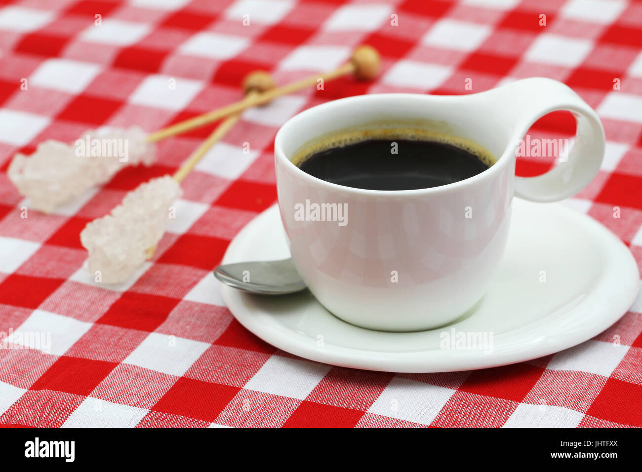 Tazza di caffè e due bastoncini di zucchero su rosso e bianco di panno a scacchi Foto Stock