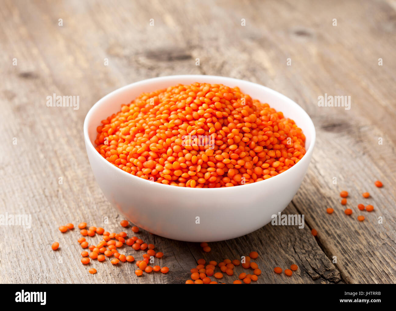 Di lenticchie rosse nella ciotola bianco sul vecchio sfondo di legno Foto Stock