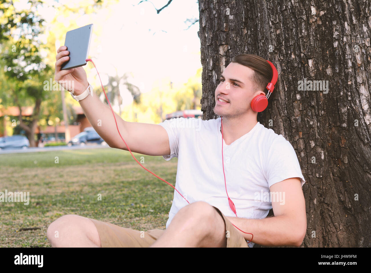Ritratto di un giovane uomo latino tenendo un selfie con tavoletta digitale. All'esterno. Foto Stock