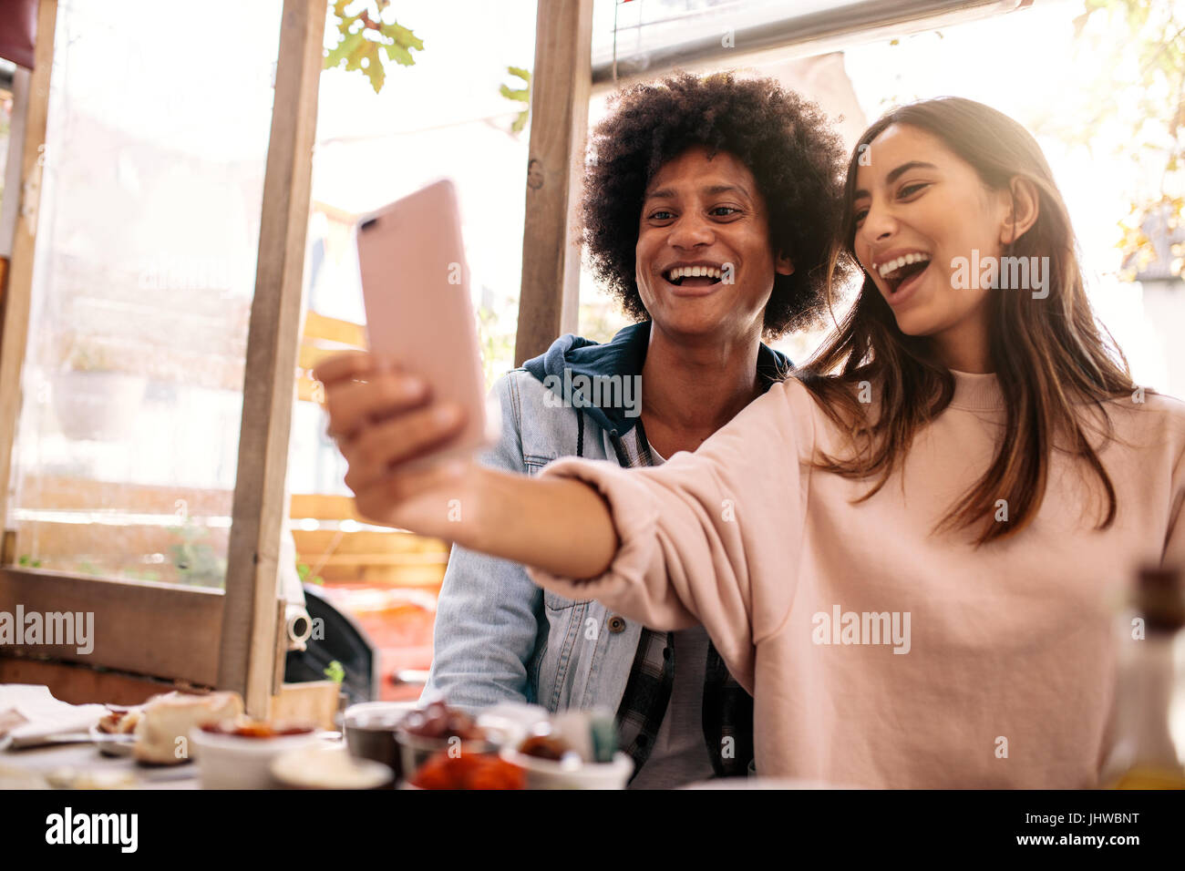 Coppia giovane seduto nella caffetteria e tenendo selfie con smart phone. Bella donna prendendo autoritratto con il suo fidanzato nel ristorante. Foto Stock