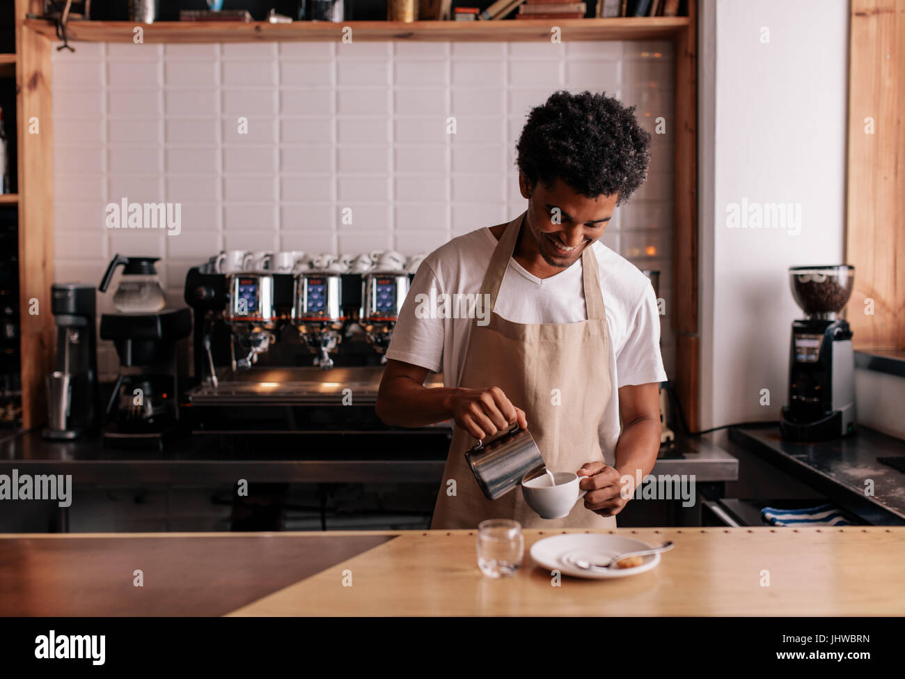 Giovane africano versando il latte nel caffè espresso. Professional barista preparazione di caffè sul contatore. Foto Stock