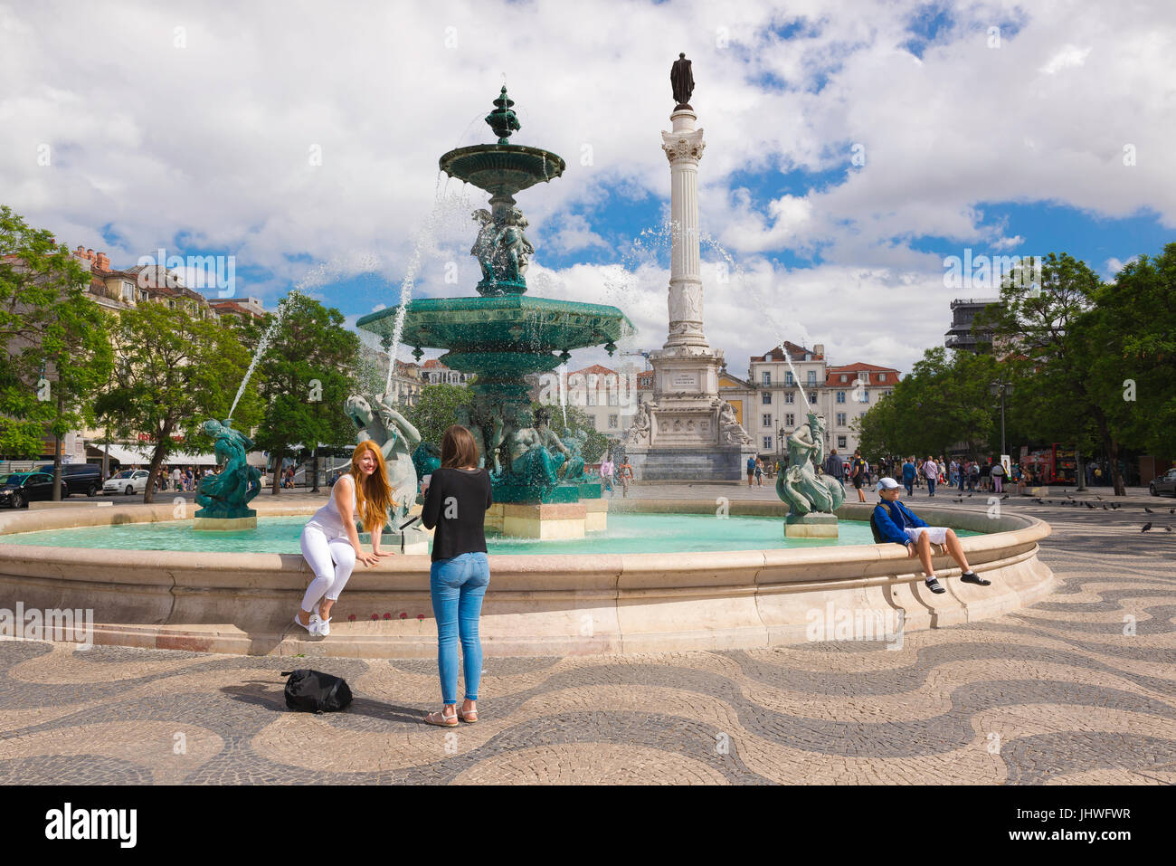 Centro di Lisbona, vista in estate di una giovane donna che posa accanto alla fontana Praca Dom Pedro LV (Rossio) mentre la sua amica scatta la sua foto, Lisbona, Foto Stock