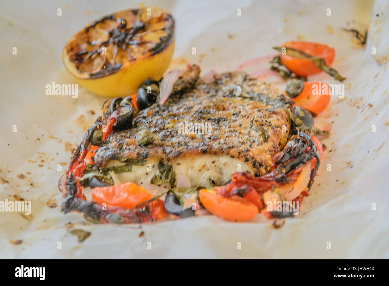 Branzino al cartoccio di mare fresca filetto di branzino cotto in carta pergamena con pomodori secchi, acciughe e capperi Foto Stock