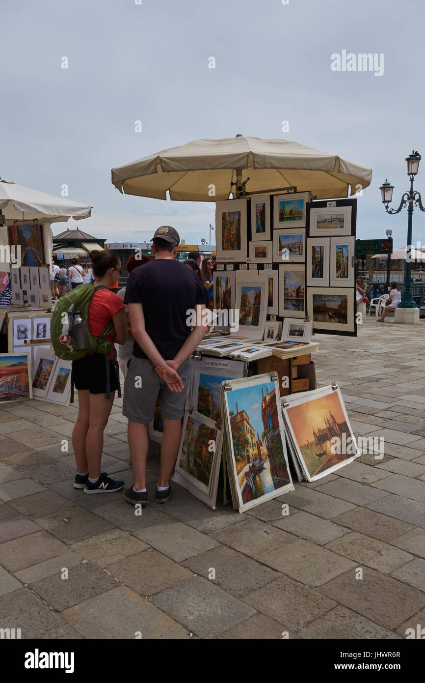 I turisti guardano dipinti in vendita presso il piccolo box. Venezia. Italia Foto Stock